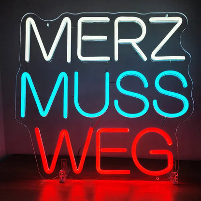Dreizeiliges Neon-Schild mit dem politischen Slogan "MERZ MUSS WEG", leuchtend in Weiß, Türkis/Blau und Rot.