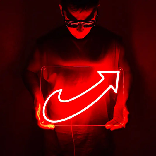 Person in dunkler Kleidung hält ein intensiv rot leuchtendes LED-Neon-Schild mit Pfeil-Motiv vor den Körper